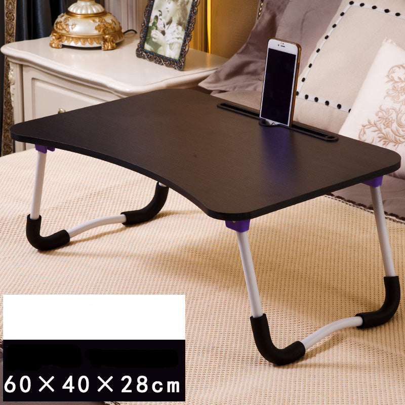 Foldable laptop desk on a bed with a phone on top, surrounded by pillows and a small table.