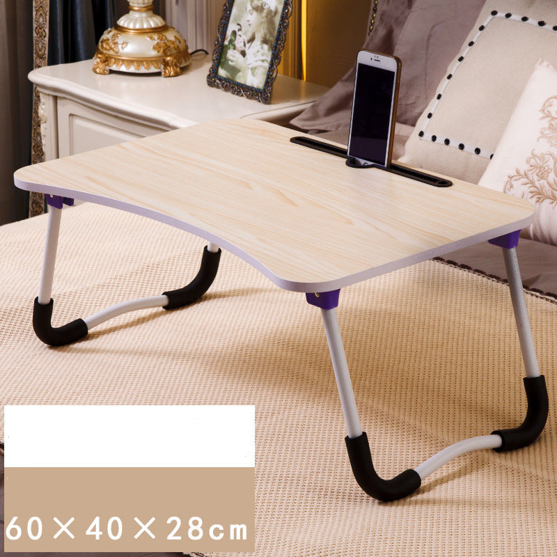 Foldable laptop desk on a bed with a phone on top, surrounded by pillows and a lamp.