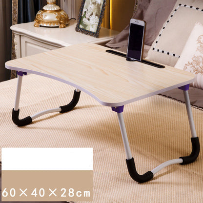 Foldable laptop desk on a bed with a phone on top, surrounded by pillows and a lamp.