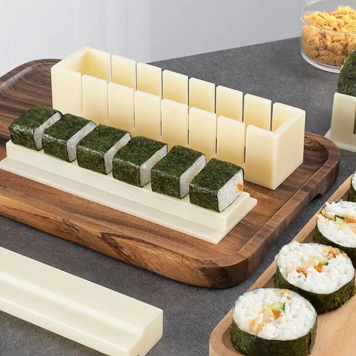 Sushi-making kit with rice blocks, nori sheets, and sushi rolls on a wooden board.